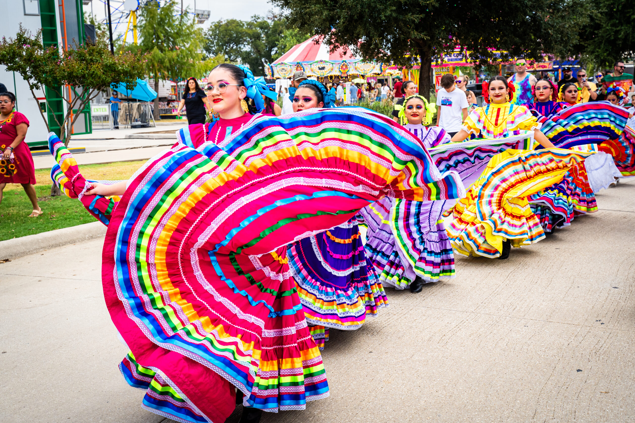 A colorful group of dancers in traditional dresses delight the Autumn Fest parade. Their vibrant stripes and ruffled skirts add a joyful rhythm to the celebration.