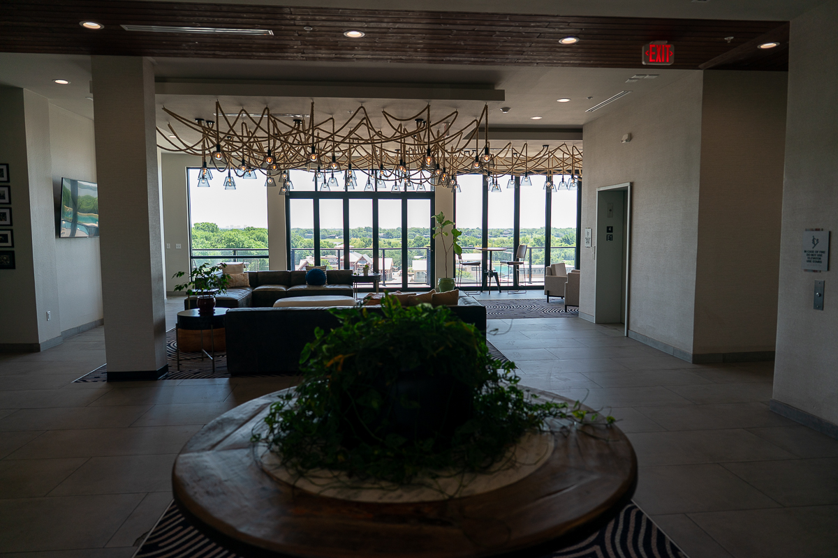 A modern lobby with seating, plants, and large windows offering a view of greenery outside.