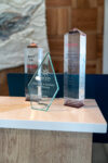 Three glass awards are displayed on a table, each engraved with text recognizing achievements for The Elm, a Ramada by Wyndham hotel.
