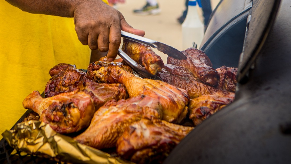 A person uses tongs to turn pieces of grilled meat cooking on a barbecue grill at Brew & Que, enjoying the perfect BBQ experience.