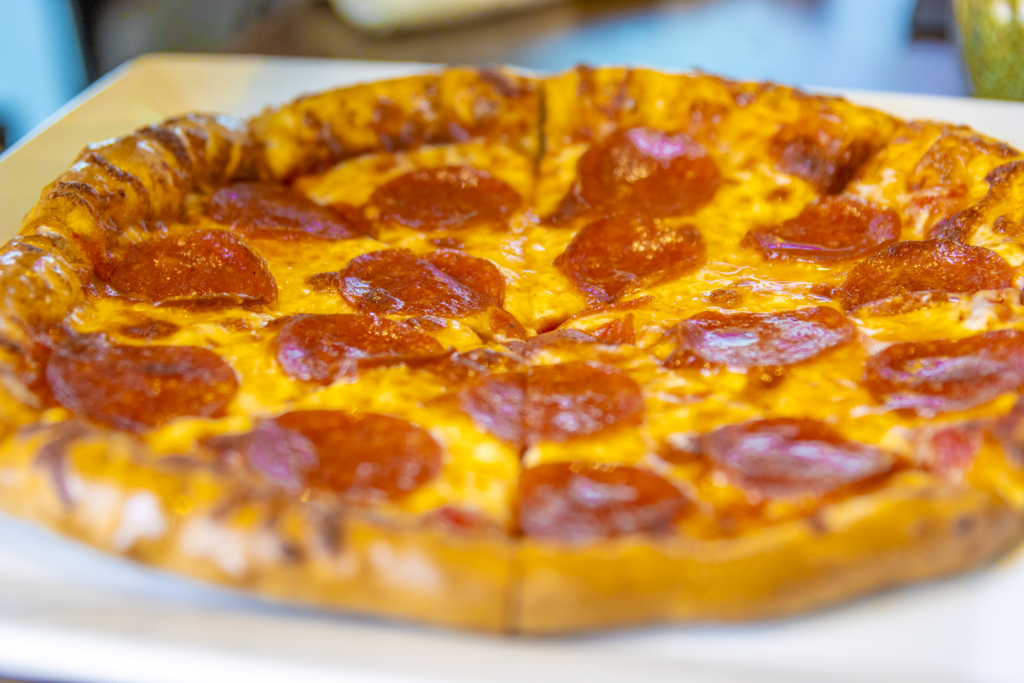 A pepperoni pizza with a golden-brown crust, topped with melted cheese and evenly distributed pepperoni slices, on a white plate.