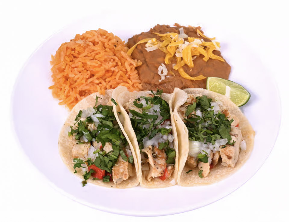 white plate of food. Including three chicken street tacos with cilantro and lime. a side of Mexican rice and refried beans.