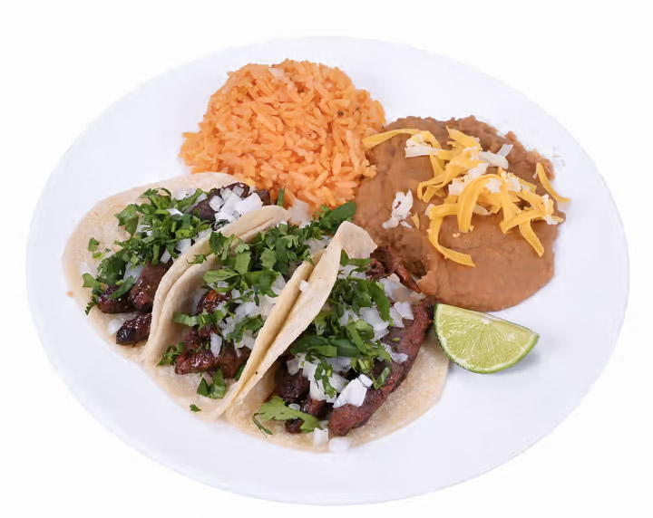 The image features a white plate filled with a delicious meal consisting of three tacos, a side of rice, and a side of beans.