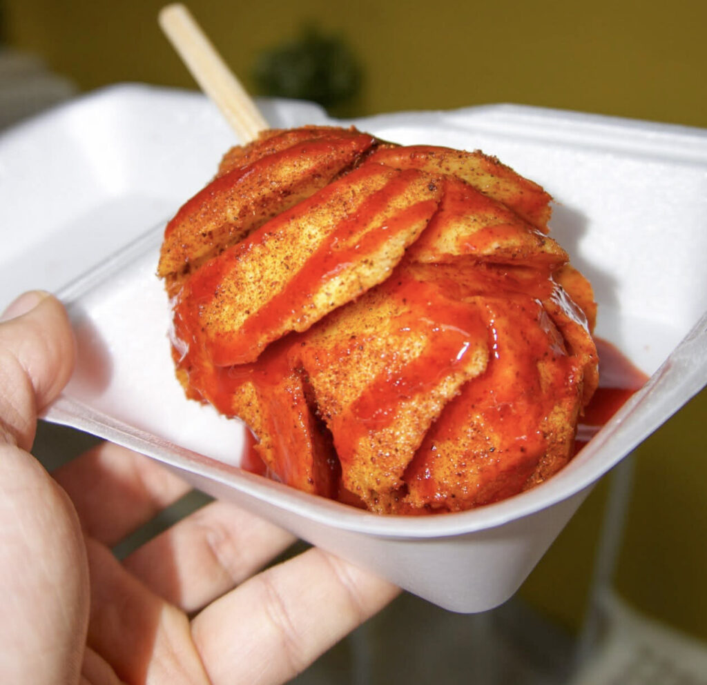 sliced mango with red seasoning in a small white to go box.