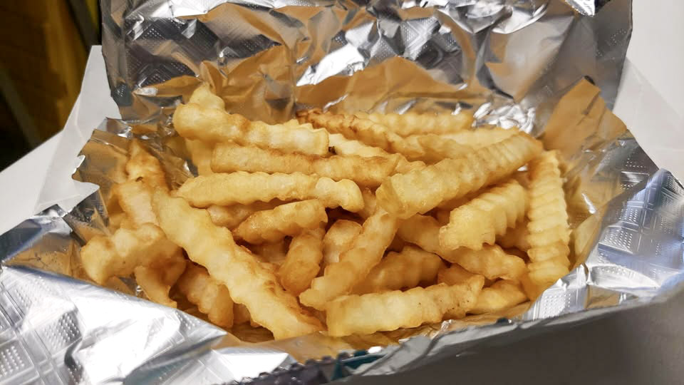 Basket of crinkle-cut fries lined with tin foil.