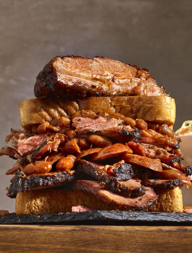 Barbeque stacked sandwich with brisket, sausage, beans with a rib on top.