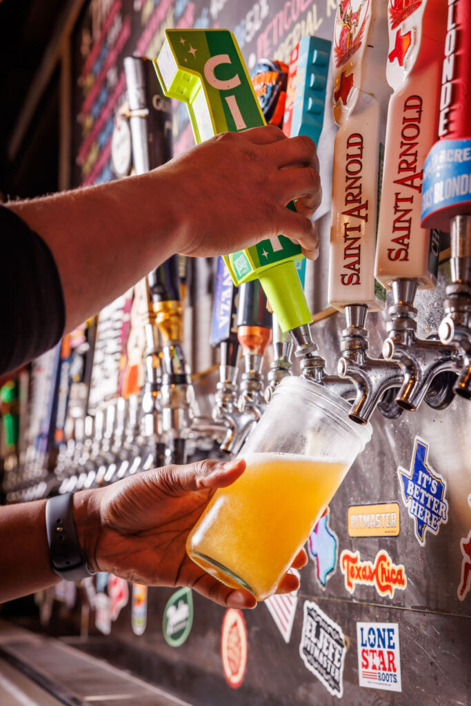 a photo of someone pulling a beer lever into a clear glass cup. with a background of many other beer taps.