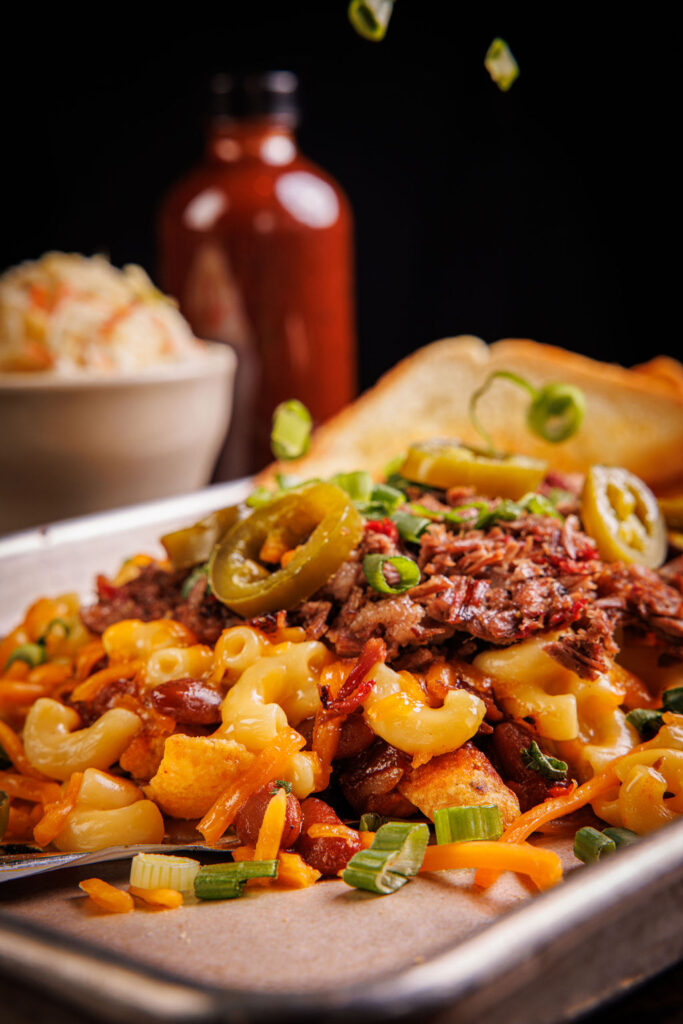 Mac and cheese topped with bacon, jalapeno, chives, and cheddar cheese, all stacked on a silver food tray.