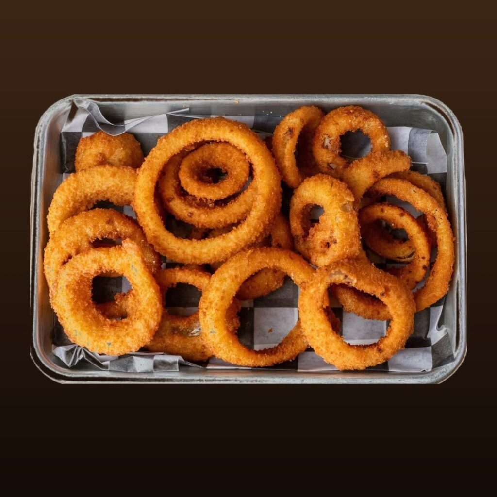 Golden-brown breaded onion rings piled in a parchment-lined metal tray against a dark background
