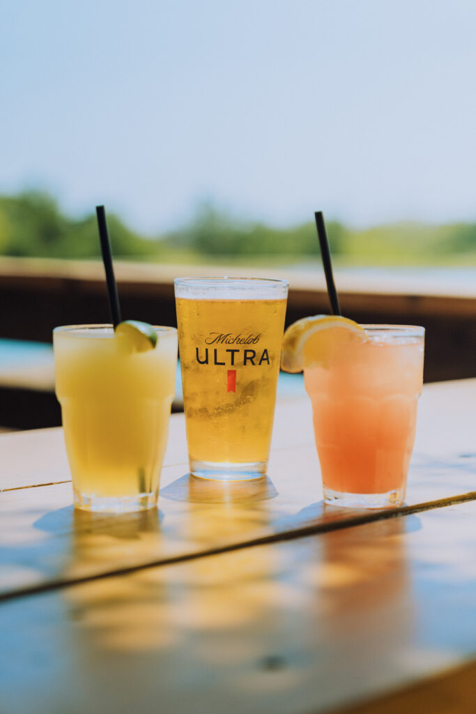 three drinks sitting on the edge of a deck. One margarita, Michelob ultra beer, and strawberry cocktail.