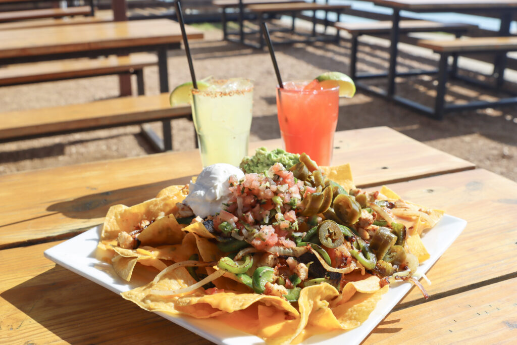 plate of giant nachos on a table sitting in front of two cocktails.