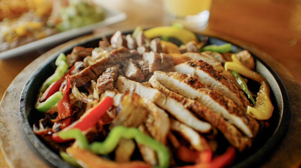 a hot plate of chicken fajita's with peppers and onions.