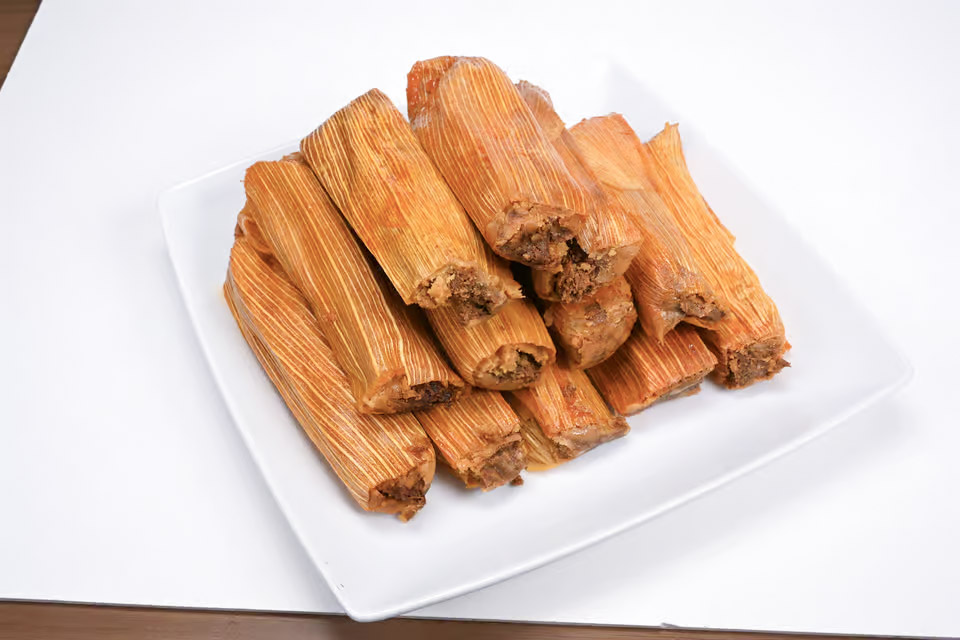 The image features a white plate filled with a delicious assortment of food. The plate is topped with a variety of tamales